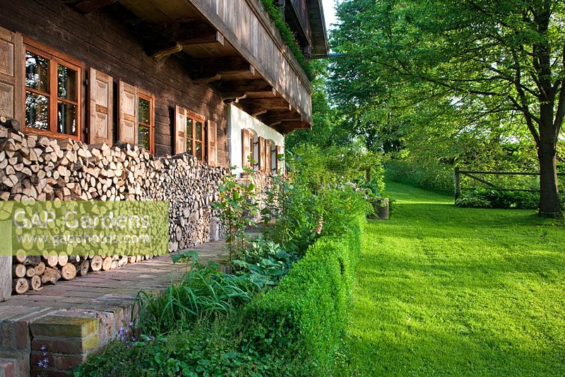 Devant une maison de campagne traditionnelle dans le sud de l'Allemagne avec balcon en bois, volets, une pile de bois et une haie de Buxus basse