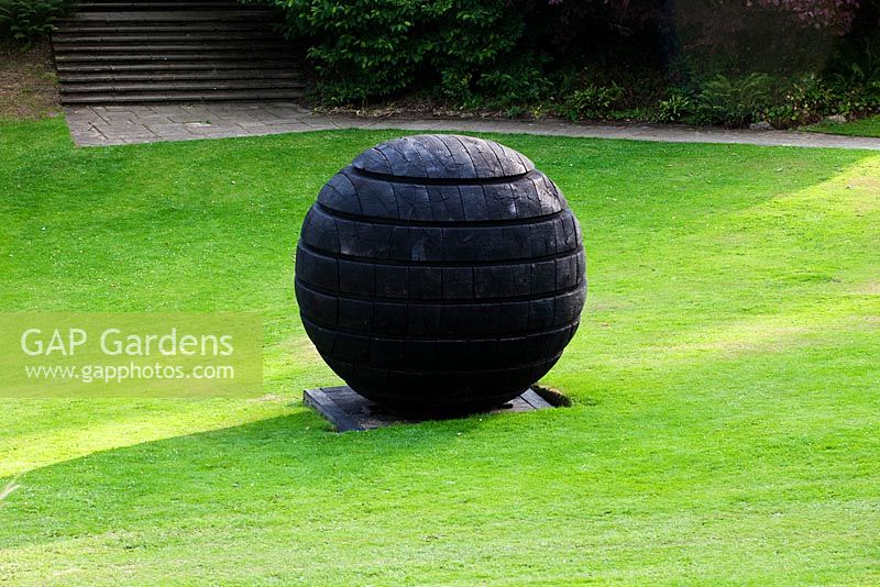 Dartington Hall, Devon. Jardin historique de catégorie II. Juillet. 'Black Sphere' de David Nash - prêté par le Yorkshire Sculpture Park. (Under the Tiltyard)