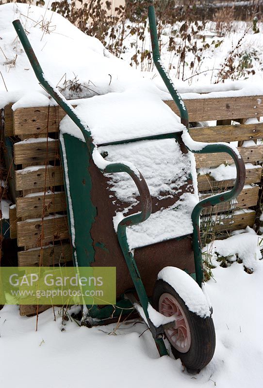 Brouette couverte de neige à côté de tas de compost en hiver