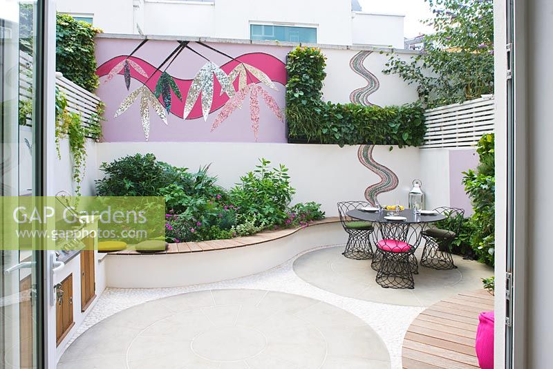 Petit jardin patio avec terrasse en bois, chaises roses, mosaïque par Celia Gregory, Londres.