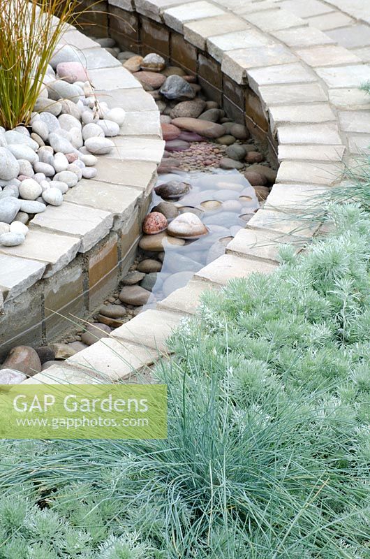 Festuca glauca 'Intense Blue' mélangé à Artemisia schmidtiana, à côté d'un ruisseau rempli de galets - LOROS Hospice Garden of Light and Reflection, médaille d'argent, RHS Hampton Court Flower Show 2011