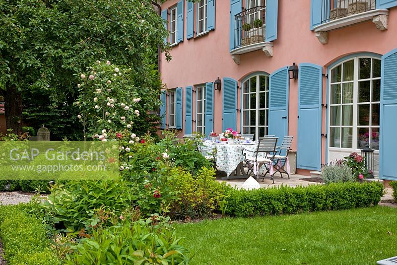 La grande terrasse avec salon de jardin en bois vue du jardin, avec Buxus - Boîtes sphères et Rosa 'Pierre de Ronsard' sur arc - Sac à main Garde, Freising, Allemagne