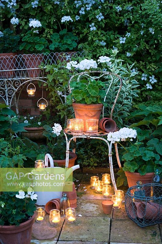 Photophore bocal en verre et géraniums blancs en pots dans un jardin blanc
