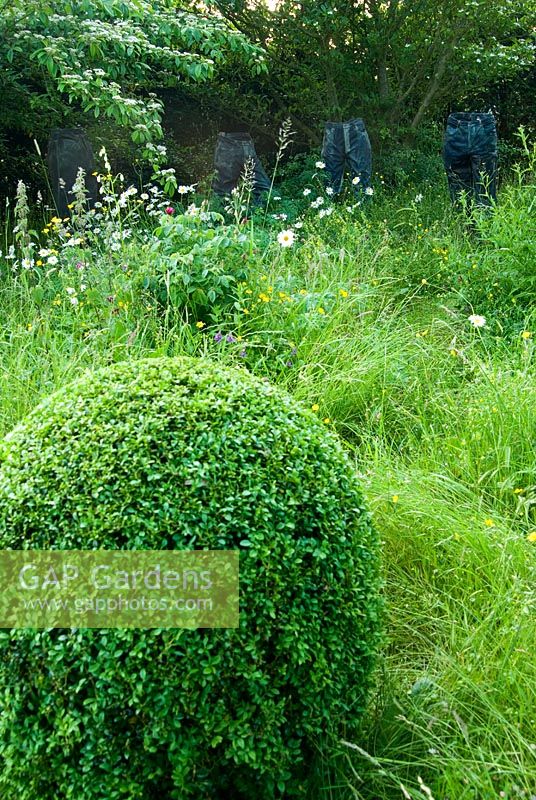 Installation sculpturale d'un jean recouvert de résine, fabriqué par Tim Hobson, dans une zone de longues herbes fleuries et de Buxus-Box clipsé. Jardin privé, Dorset, UK