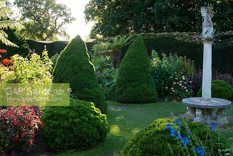 Le jardin cadran solaire avec le soleil de fin d'après-midi éclairant les fougères arborescentes, les pics coniques et les plantes herbacées exotiques, y compris les Salvias, les Dahlias et les Ricinus - Exbury Gardens, Exbury, Hants, UK