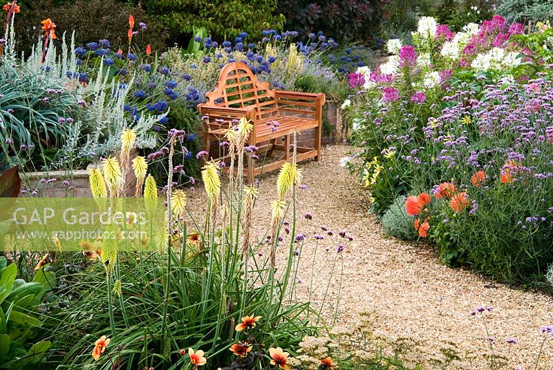 Des chemins de gravier à travers le jardin englouti sont bordés d'une masse de vivaces et d'annuelles colorées, y compris Cleomes, Agapanthus, Eucomis, Dahlias, Verbena bonariensis et Kniphofias - Isle of Wight, Royaume-Uni