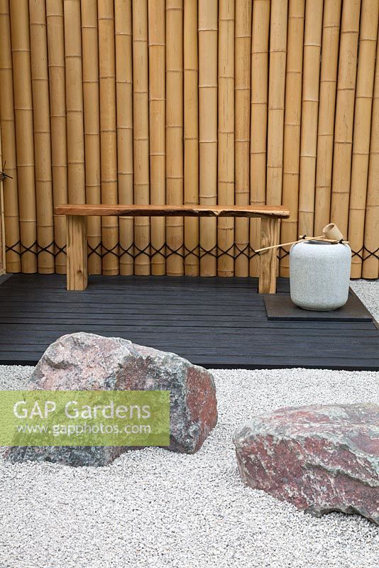 Un coin salon avec des rochers et un chemin de gravier soutenu par une clôture en bambou dans le jardin à thème japonais - 'Less and More' garden - RHS Hampton Court Flower Show 2011