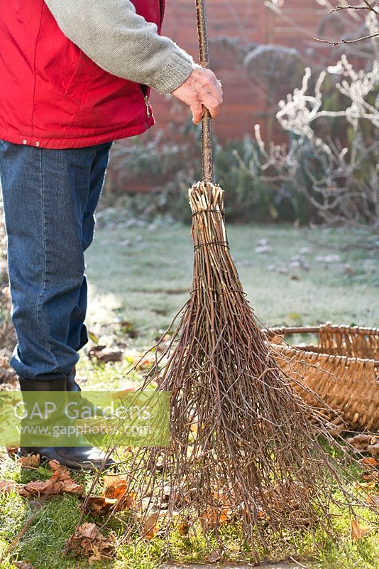 Fabrication d'un balai en bouleau - homme rangeant les feuilles de la pelouse à l'aide d'un balai en bouleau nouvellement fabriqué.