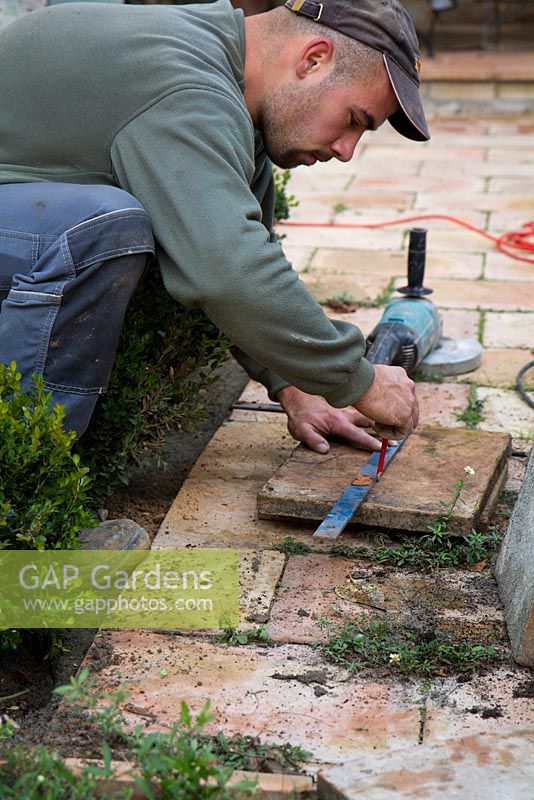 Homme marquant la tuile de jardin avant de couper avec une meuleuse d'angle pour s'adapter au plan de la terrasse du jardin.