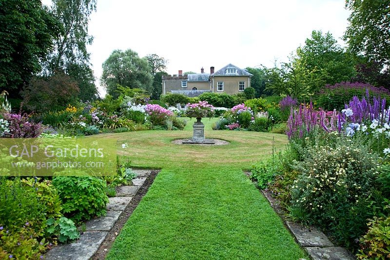 Les parterres de faucille, dans le jardin à l'ouest de la maison, avec une urne centrale et des parterres pleins de Phlox, Lythrums, Crinums et autres plantes vivaces herbacées - Old Rectory, Pulham, Dorset
