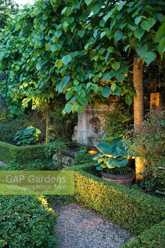 Jardin méditerranéen de style formel avec une haie basse entourant l'étang, les hostas en pots, l'éclairage, les chemins de gravier et les limes blanchies - Madrid, Espagne