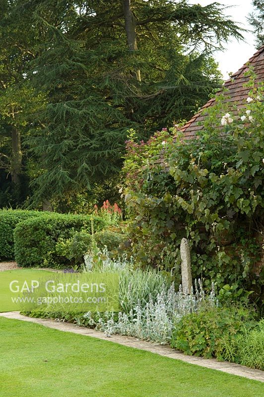 Bâtiment de jardin en toit de briques et de tuiles avec parterre de fleurs bordé par un chemin de dalle de pavage. Les plantes comprennent - Lavandula et Stachys byzantina - Mannington Hall, Norfolk, Royaume-Uni