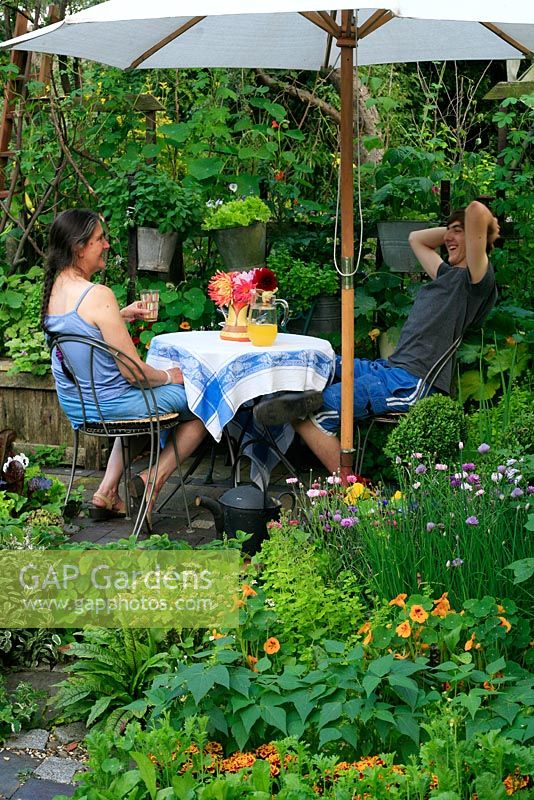 Petit potager décoratif planté d'herbes, de fleurs, de fruits et légumes qui comprend une petite table et des chaises et des pots suspendus remplis de légumes à salade