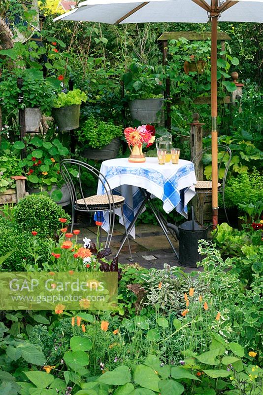 Petit potager décoratif planté d'herbes, de fleurs, de fruits et légumes, une petite table et des chaises et des pots suspendus remplis de légumes à salade