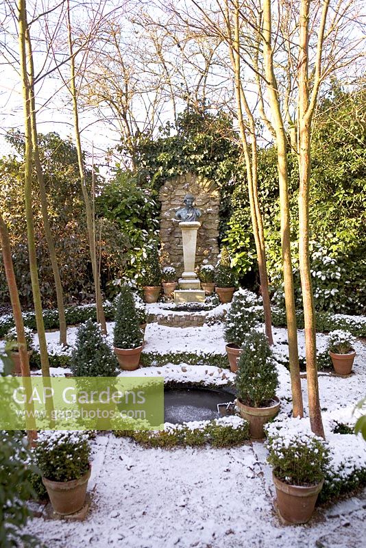 Jardin formel avec étang circulaire et conifères dans des pots en terre cuite - la vieille école, Great Bentley, Essex en janvier