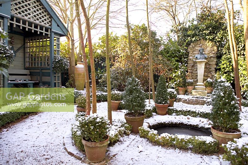 Jardin à la française avec maison d'été, étang circulaire et conifères dans des pots en terre cuite - The Old School House, Great Bentley, Essex en janvier