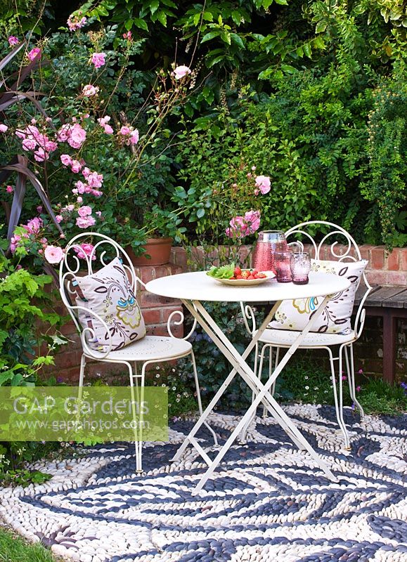 Patio avec sol en mosaïque de galets, table et chaises en métal blanc avec coussins