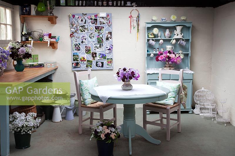Le studio de fleurs avec des compositions florales, une vieille commode avec des vases vintage, des panneaux d'affichage, des cruches et des seaux en émail, une table et des chaises - Vert et magnifique