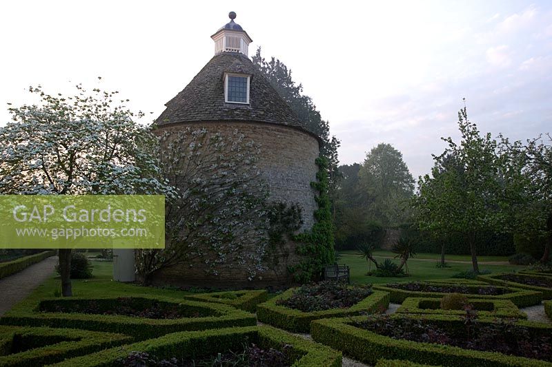 Jardin Pigeon House avec pigeonnier, 1685, et parterre avec Cornus nuttallii et de nouvelles feuilles rouges de roses de thé hybrides. Rousham House