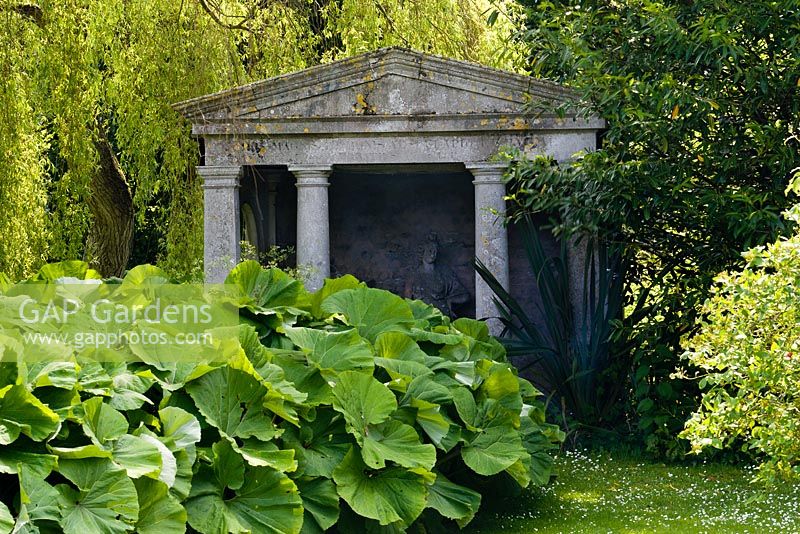 Temple dans la partie humide du jardin avec Petasites alba - Butterburr en face. Salix x sepulcralis var. chrysocoma - saule pleureur derrière le temple. Statue de 'l'architecture' à l'intérieur du temple