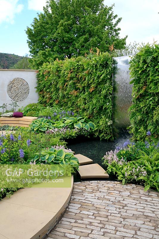 Fougères poussant verticalement sur un mur avec une cascade d'eau en acier inoxydable alimentant un étang peu profond. Spring Show 2012. Médaille d'or et Best Show Garden.