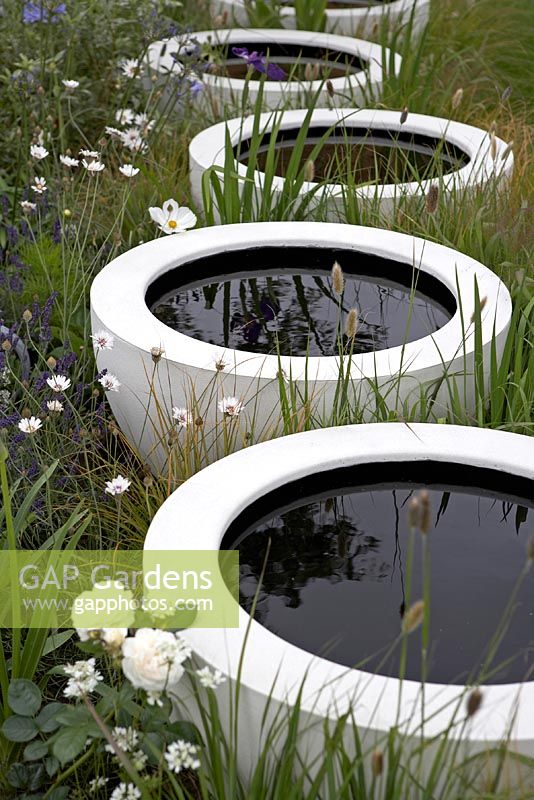 Récipients blancs circulaires contenant des mares d'eau sombres dans une plantation de style pré - Célébration et jubilation - RHS Hampton Court Flower Show 2012