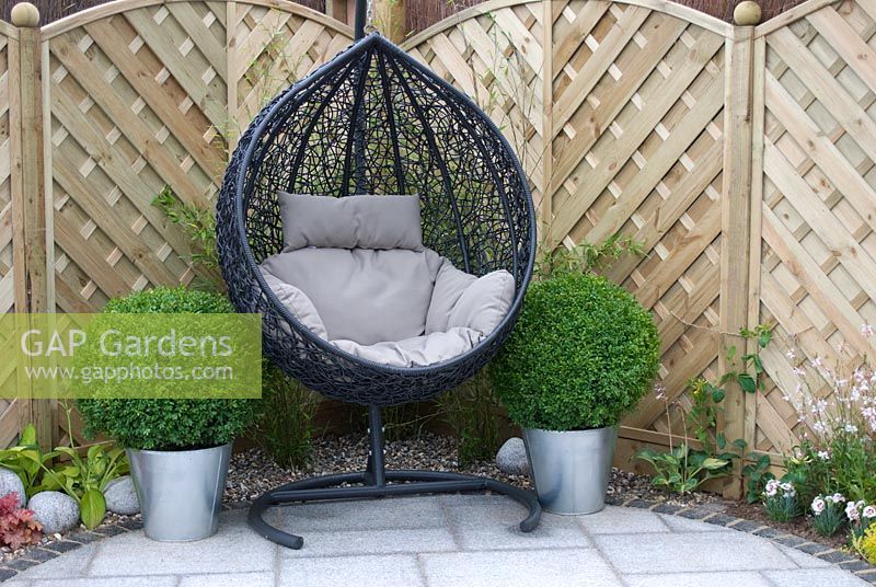 Patio circulaire avec chaise circulaire suspendue et clôture décorative en bois derrière dans le jardin 'No Corners Just Curves', RHS Tatton Flower Show 2012