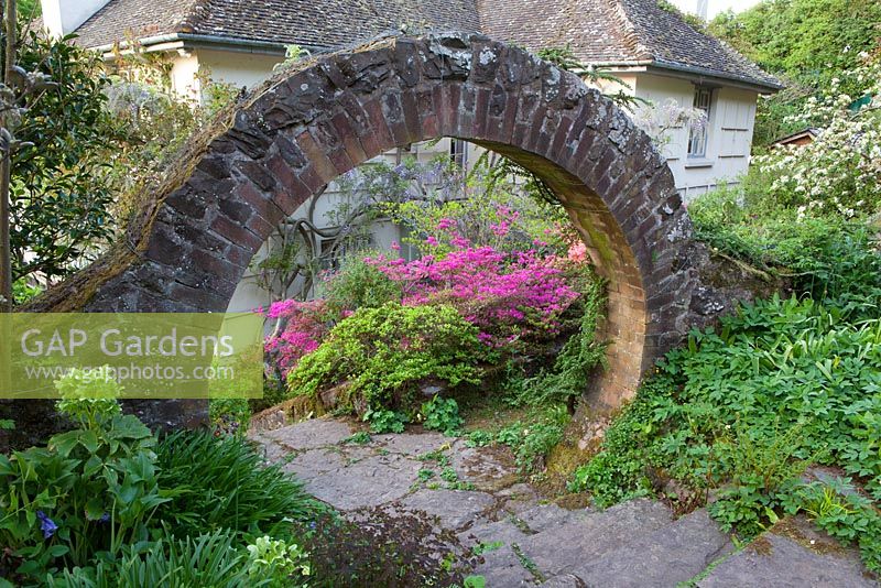 Regardant à travers l'arc circulaire vers les azalées et les glycines par la maison à Greencombe Gardens, Somerset