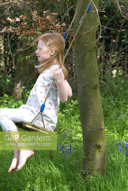 Fille sur une balançoire dans un bois avec Hyacinthoides non-scripta - Bluebells anglais fin avril