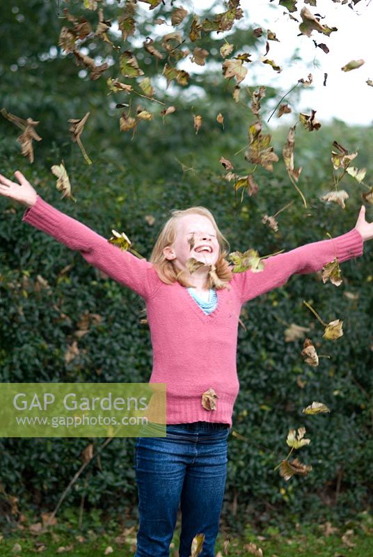 Jeune fille jetant et s'amusant avec les feuilles d'automne, octobre