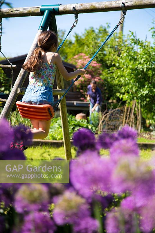 Jeune fille jouant sur la balançoire, Allium aflatunense en premier plan