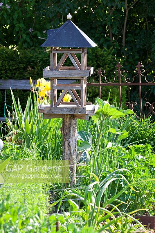 Maison d'alimentation d'oiseaux en bois dans un potager, clôture de jardin en fer antique en arrière-plan