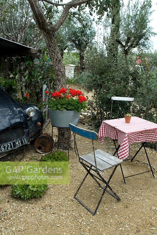 Table et chaises dans le jardin d'un café français rural, avec des oliviers, des géraniums rouges dans un bain galvanisé et une vieille voiture Citroën - Garden Show 'Reposer Vos Roues / Rest your Wheels', Gold Award, Malvern Spring Show 2013