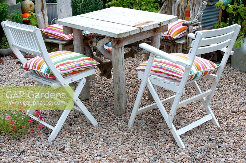 Coin salon avec petite table carrée en bois flotté et chaises rembourrées en gravier dans le coin du jardin du chalet
