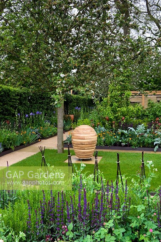 Jardin avec potager intégré, pelouse avec sculpture et allées entre parterres et parterres mixtes