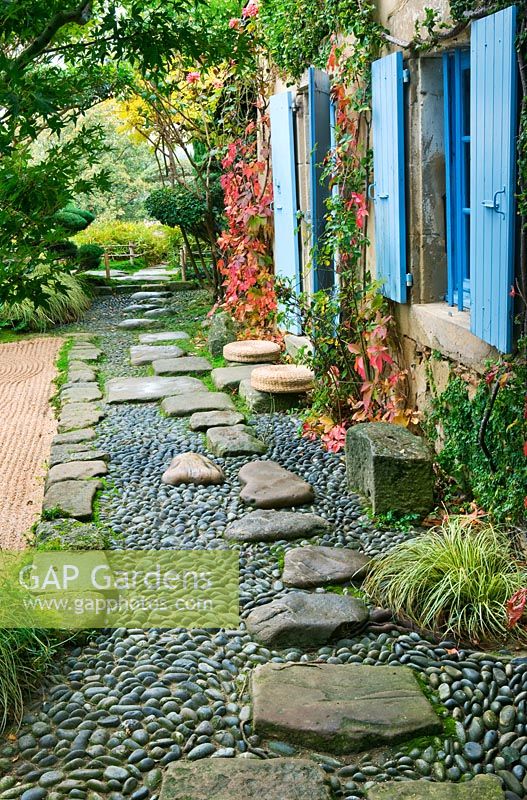 Jardin de style japonais - vue sur le côté est de la maison avec volets bleus, chemin avec galets et rochers et jardin de gravier