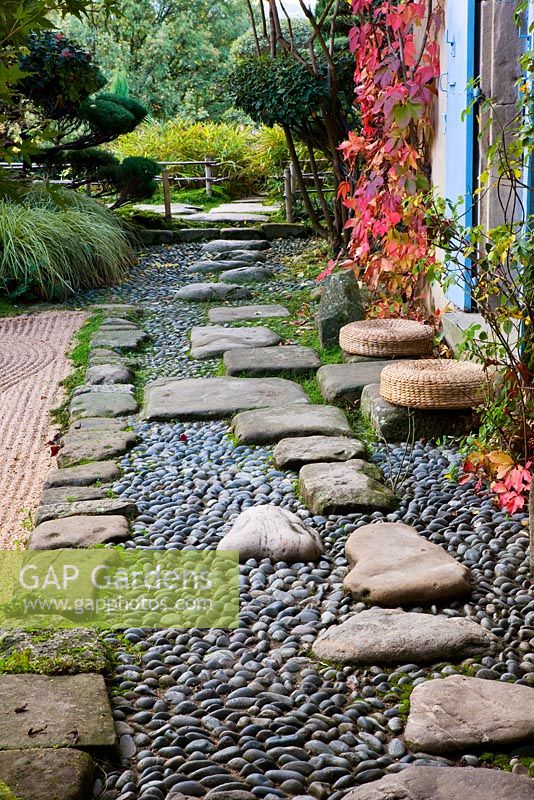 Jardin de style japonais - vue sur le côté est de la maison avec volets bleus, chemin avec galets et rochers et jardin de gravier