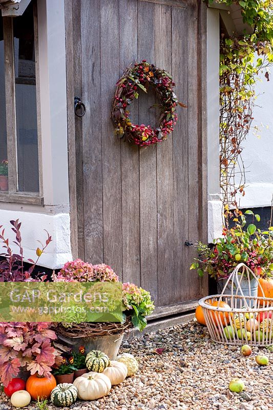 Décoration rustique d'automne à l'extérieur de la porte du chalet avec couronne, hortensias, courges, pommes