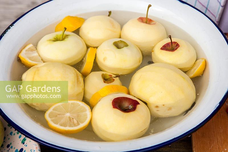 Avec des tranches de citron, des pommes fraîchement pelées nagent dans un bol en émail blanc, Malus domestica