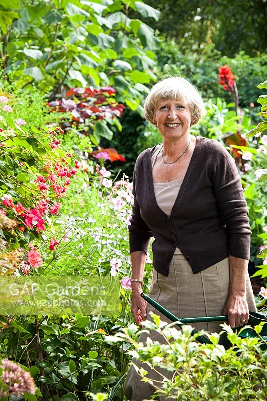 Portrait du propriétaire de Janet Daniel arrosant son jardin. Les plantes comprennent le fuchsia, l'aster et l'anémone japonaise