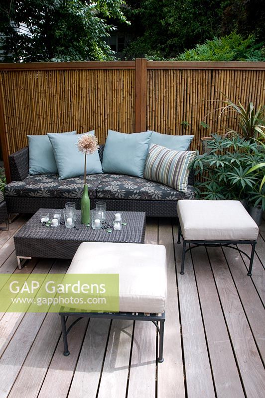 Coin salon extérieur sur terrasse en bois, avec clôture en bambou.