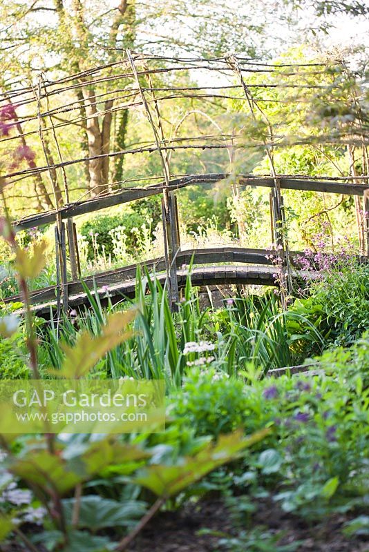 Pont voûté de style tissé naturaliste sur l'étang au début de l'été