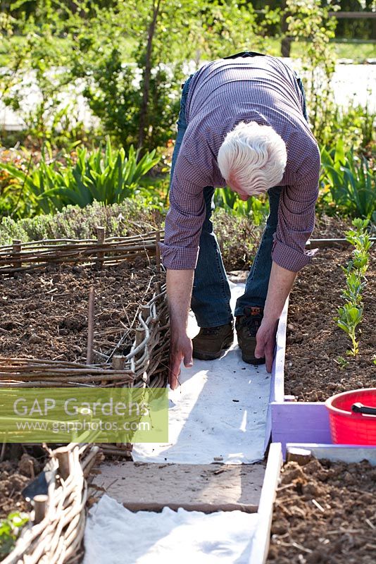 Homme construisant un chemin de gravier dans le potager. Pose de feutre pour éviter les mauvaises herbes.