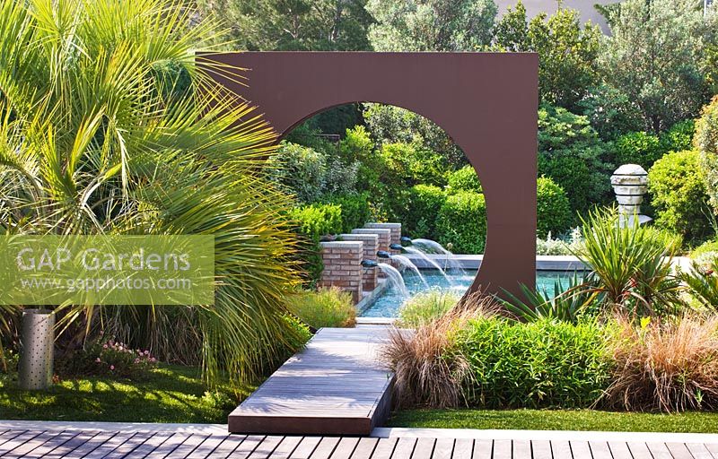 Jardin moderne et contemporain - terrasse en bois, plan d'eau, cercle 'oculus' en métal et piscine. Les Confines, Provence, France