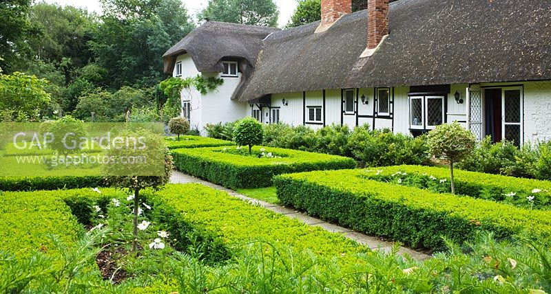 La chaumière vue depuis le jardin à la française de haies de buis taillées et de sucettes d'ifs panachés