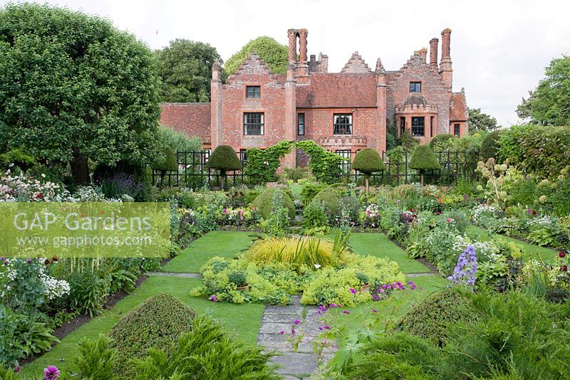 Jardin submergé formel en été avec Alchemilla mollis, Geranium, Rosa, Papaver, Feverfew avec Manor House derrière. Chenies Manor, Buckinghamshire