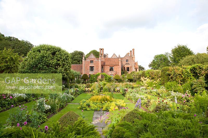 Jardin submergé formel en été avec Alchemilla mollis Geranium Rosa Papaver Feverfew avec Manor House derrière. Chenies Manor, Buckinghamshire