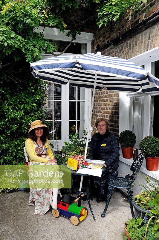 Deux femmes assises à une table sous un parasol dans un jardin ouvert sous le National Garden Scheme NGS dans le London Borough of Hackney et vendant des billets pour l'événement.
