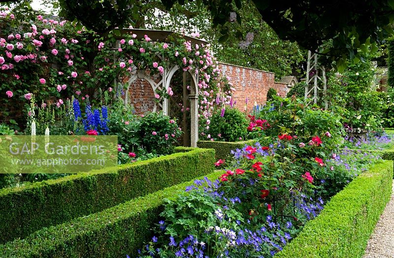 Un jardin clos anglais classique avec des parterres de fleurs ornementaux à bords arrondis, des rosiers grimpants et une tonnelle décorative en bois - Seend, Wiltshire