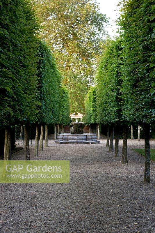 Allée de style français de chaux pêchée menant à travers l'axe du jardin avec élément d'eau orné central et porte à l'extrémité - Seend, Wiltshire